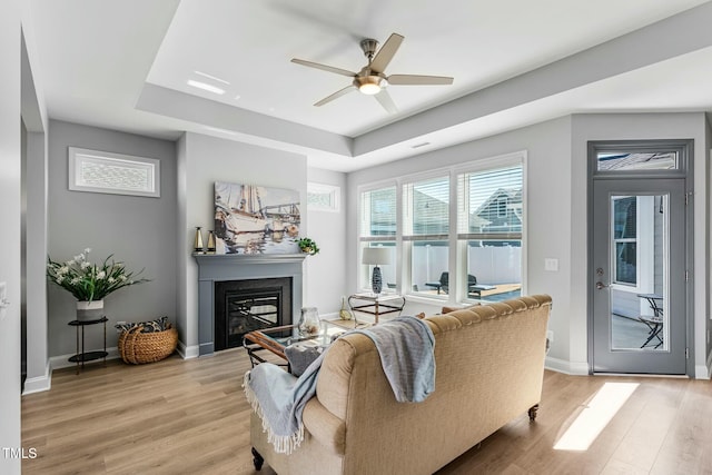 living area featuring a glass covered fireplace, light wood-style flooring, and a tray ceiling