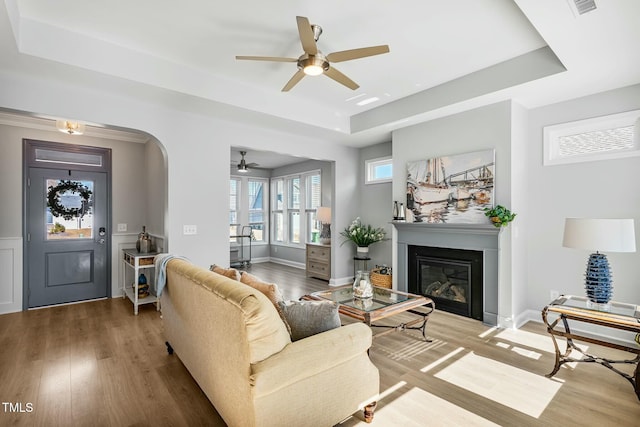 living room with arched walkways, a raised ceiling, wood finished floors, and a glass covered fireplace