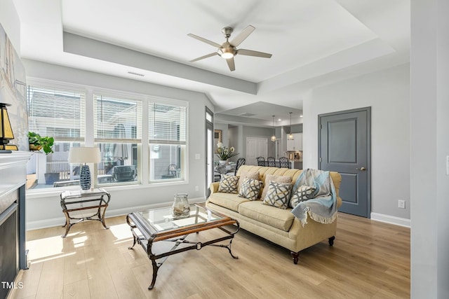 living room with visible vents, baseboards, a raised ceiling, a ceiling fan, and light wood-style floors