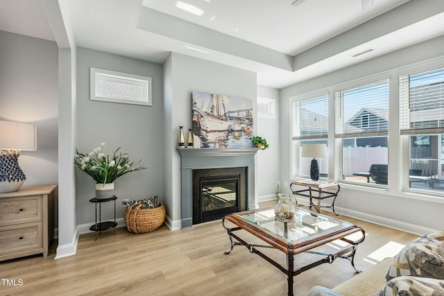 living area with light wood-type flooring, a raised ceiling, a glass covered fireplace, and baseboards