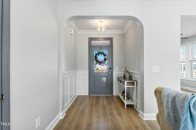 entryway featuring arched walkways, a decorative wall, light wood-style floors, ornamental molding, and wainscoting