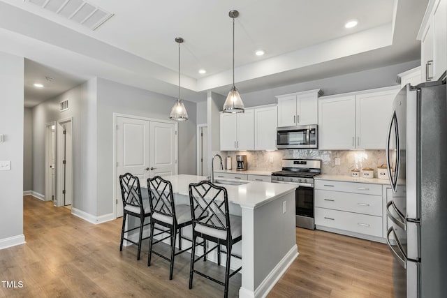 kitchen with stainless steel appliances, a sink, white cabinets, light countertops, and an island with sink