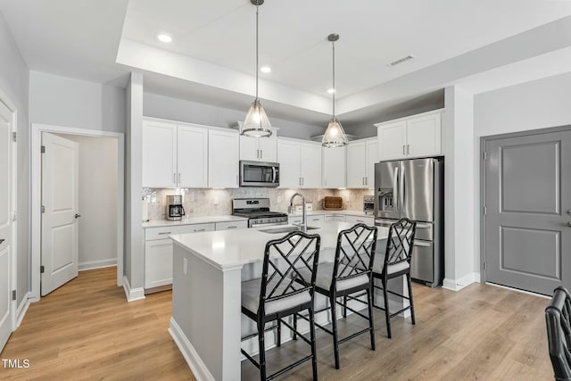 kitchen with a center island with sink, light countertops, appliances with stainless steel finishes, white cabinets, and a sink