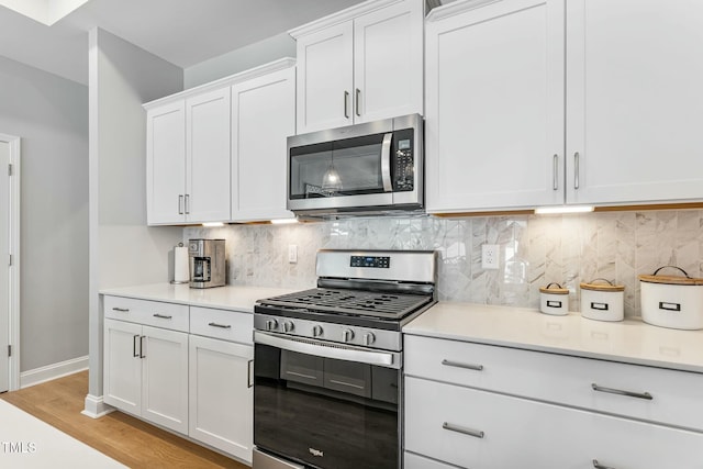 kitchen with stainless steel appliances, light countertops, backsplash, white cabinetry, and light wood-type flooring