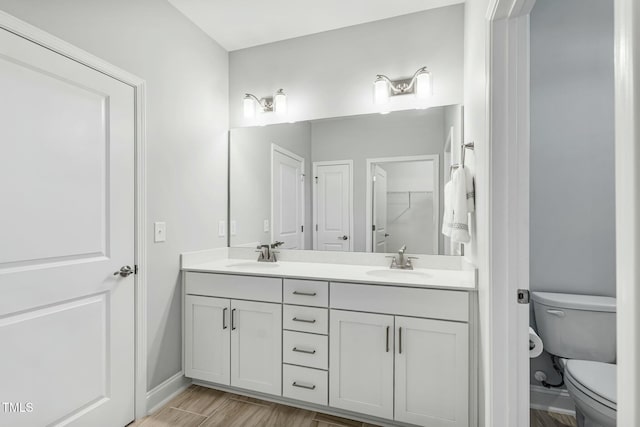 bathroom with wood finished floors, a sink, toilet, and double vanity