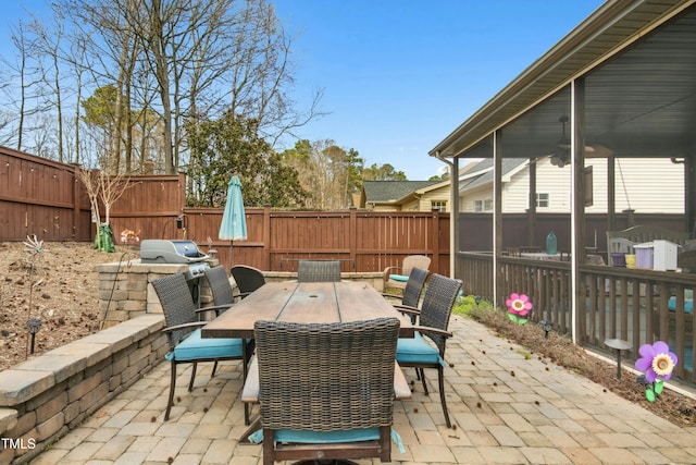 view of patio / terrace featuring a sunroom, a fenced backyard, a grill, and outdoor dining area