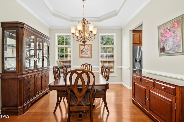 dining space featuring ornamental molding, a raised ceiling, wood finished floors, and a chandelier