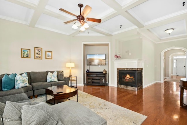 living area with arched walkways, beam ceiling, wood finished floors, coffered ceiling, and baseboards