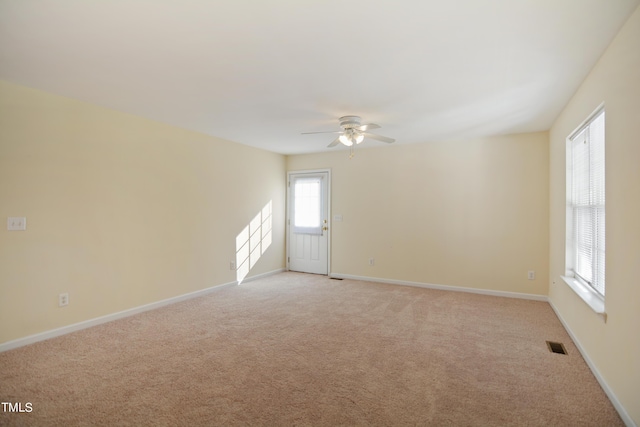 spare room featuring light colored carpet, ceiling fan, visible vents, and baseboards