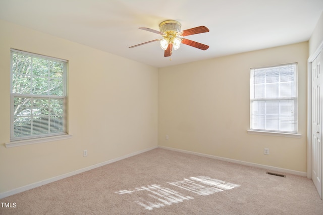 carpeted empty room featuring baseboards, a ceiling fan, visible vents, and a healthy amount of sunlight