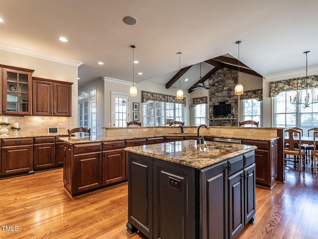 kitchen featuring vaulted ceiling with beams, light wood-style flooring, a spacious island, a sink, and tasteful backsplash