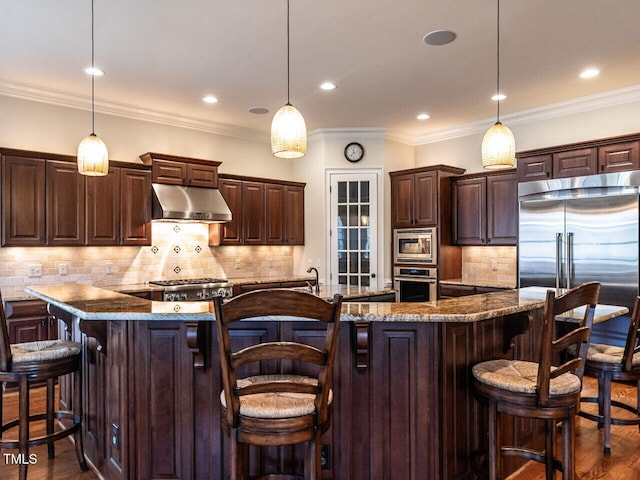 kitchen featuring dark wood-type flooring, dark brown cabinetry, under cabinet range hood, and built in appliances