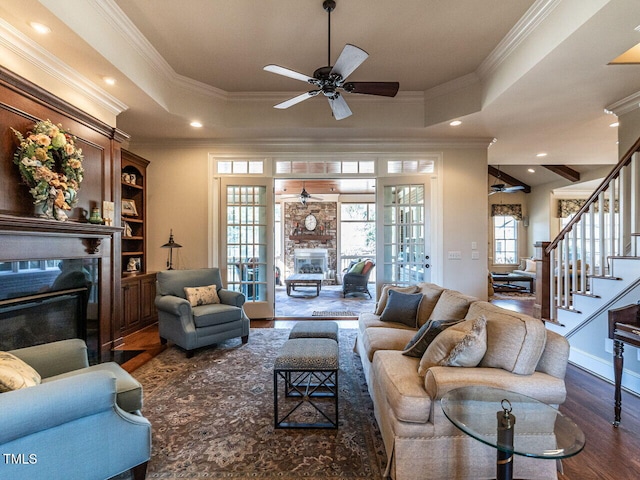 living area with wood finished floors, a fireplace with flush hearth, ornamental molding, stairway, and a raised ceiling