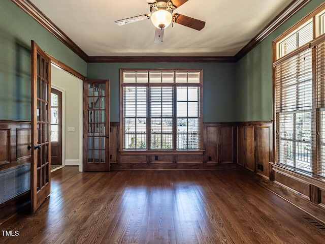 spare room with a healthy amount of sunlight, ornamental molding, dark wood-type flooring, and wainscoting