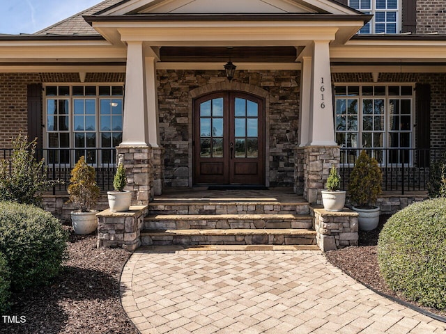 doorway to property with a porch, stone siding, and french doors