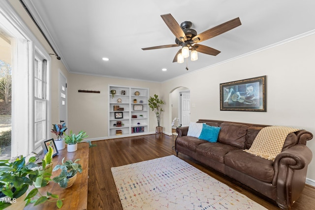 living room featuring arched walkways, wood finished floors, a ceiling fan, baseboards, and crown molding