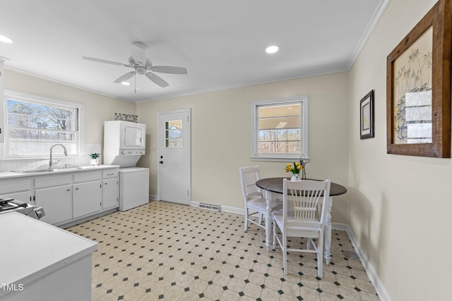 kitchen featuring stacked washer and clothes dryer, ornamental molding, light countertops, light floors, and a sink