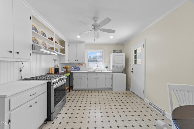 kitchen featuring stacked washer and clothes dryer, light floors, stainless steel gas range, under cabinet range hood, and open shelves