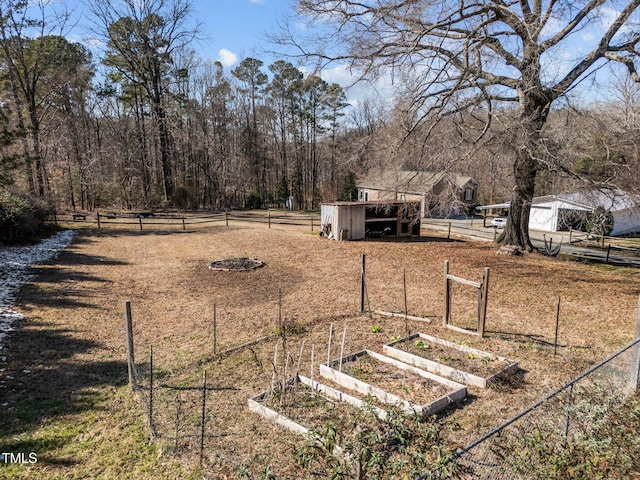 view of yard featuring an outbuilding, a rural view, a vegetable garden, and fence