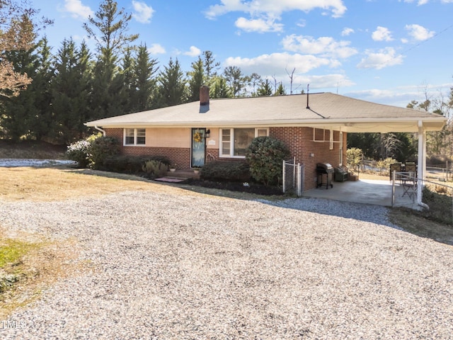 ranch-style house with a carport, brick siding, driveway, and a chimney