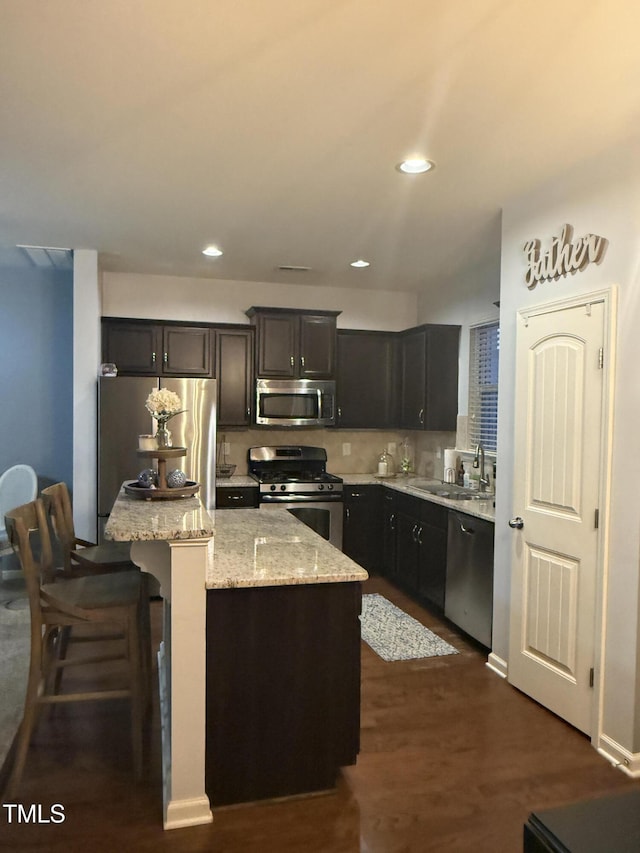 kitchen with light stone counters, stainless steel appliances, a kitchen island, a sink, and backsplash