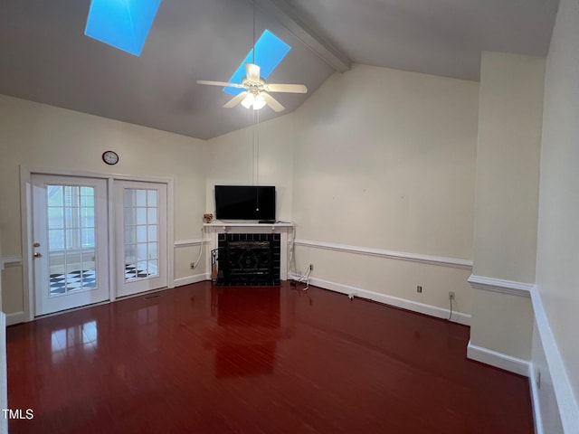 unfurnished living room with a fireplace, a ceiling fan, baseboards, lofted ceiling with skylight, and dark wood finished floors