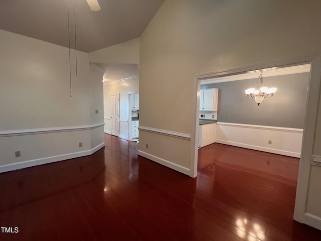 spare room with dark wood-style floors, ornamental molding, vaulted ceiling, baseboards, and ceiling fan with notable chandelier