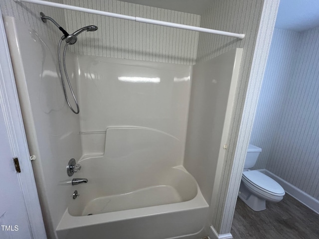 bathroom with toilet, washtub / shower combination, baseboards, and wood finished floors