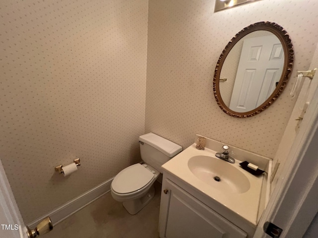 bathroom featuring baseboards, vanity, toilet, and wallpapered walls