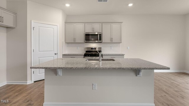 kitchen featuring appliances with stainless steel finishes, an island with sink, gray cabinets, and light stone counters