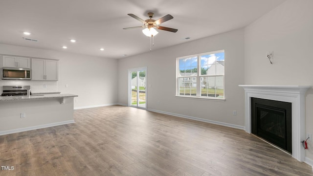 unfurnished living room with a fireplace, wood finished floors, visible vents, and baseboards