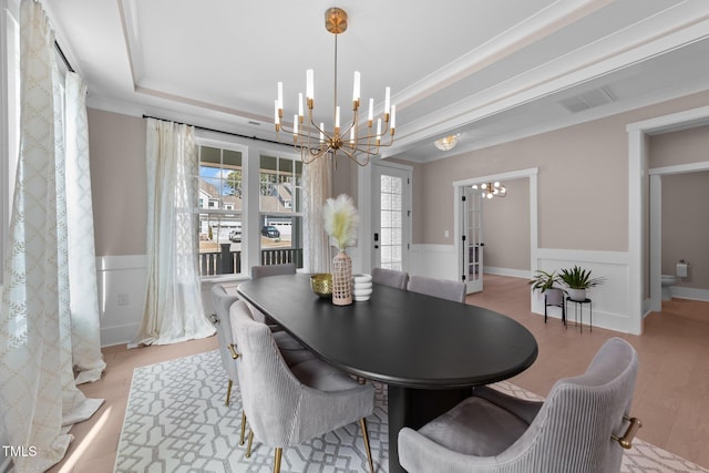 dining area featuring a wainscoted wall, light wood-style flooring, ornamental molding, an inviting chandelier, and a tray ceiling