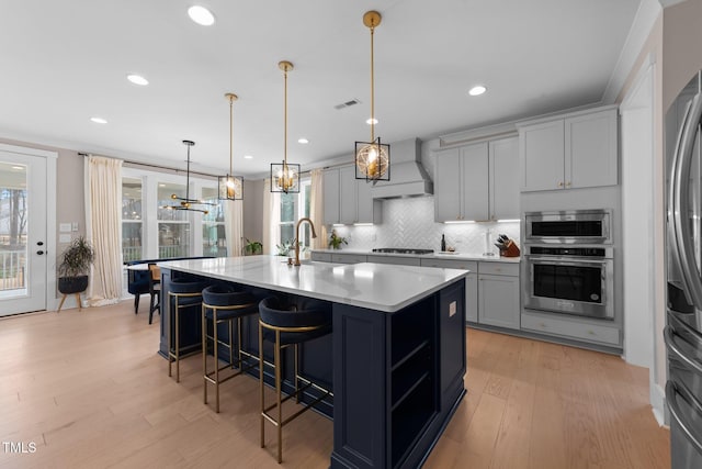 kitchen featuring premium range hood, light countertops, appliances with stainless steel finishes, a center island with sink, and pendant lighting