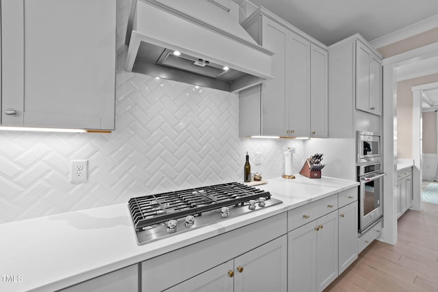 kitchen with light wood-type flooring, custom exhaust hood, stainless steel appliances, and backsplash