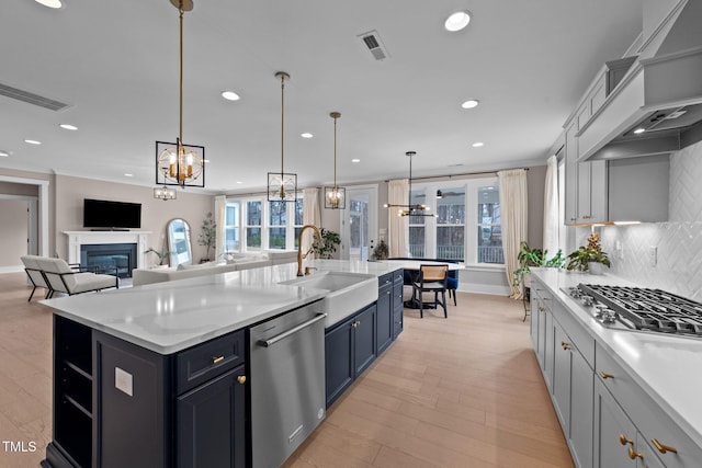 kitchen with open floor plan, hanging light fixtures, a kitchen island with sink, stainless steel appliances, and a sink