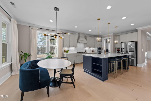 kitchen featuring decorative light fixtures, a kitchen island with sink, stainless steel appliances, gray cabinetry, and premium range hood