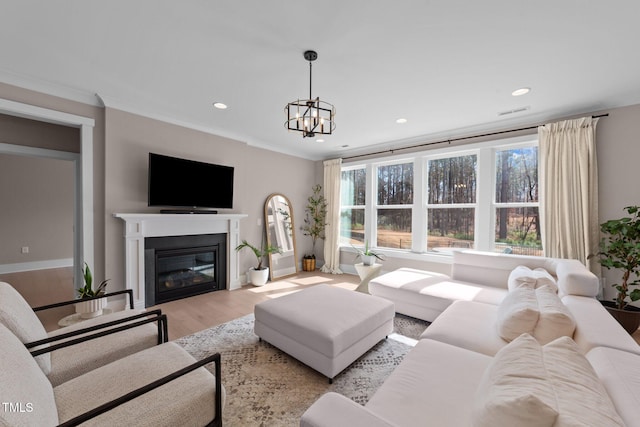 living area featuring plenty of natural light, ornamental molding, light wood-style flooring, and a glass covered fireplace