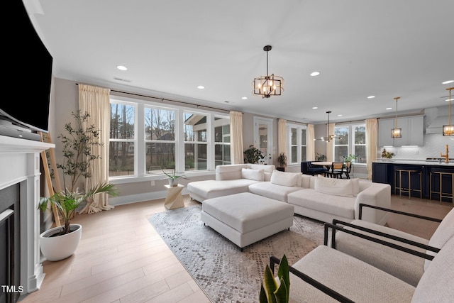 living room with light wood-type flooring, a notable chandelier, a fireplace, and recessed lighting