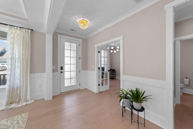 foyer with visible vents, wainscoting, light wood-type flooring, an inviting chandelier, and crown molding