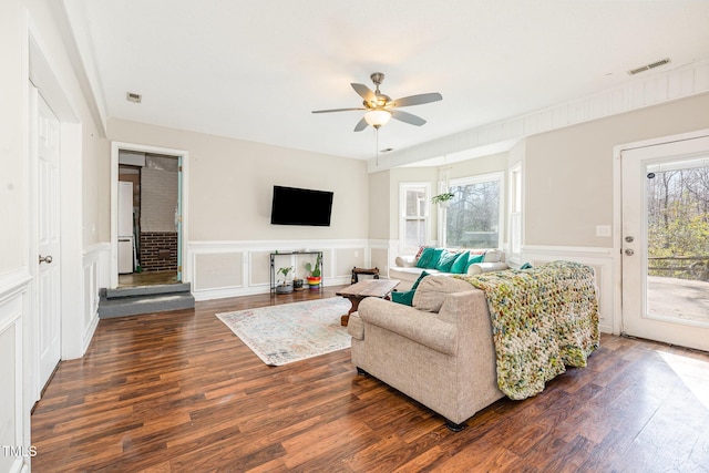 living room featuring dark wood-type flooring, visible vents, ceiling fan, and a decorative wall