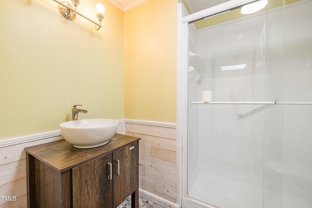 bathroom with a wainscoted wall, wood walls, a sink, and a stall shower