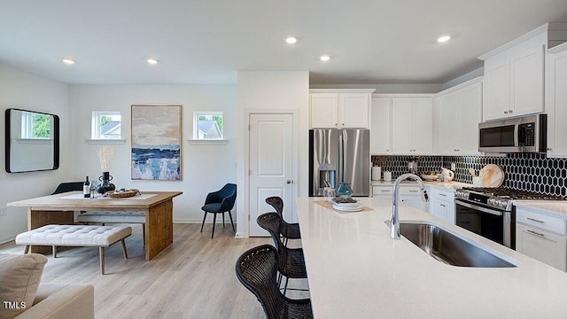 kitchen with a sink, white cabinets, light countertops, appliances with stainless steel finishes, and light wood-type flooring