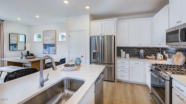 kitchen with light wood finished floors, white cabinets, appliances with stainless steel finishes, light countertops, and a sink