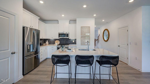 kitchen with stainless steel appliances, a sink, white cabinets, light countertops, and an island with sink