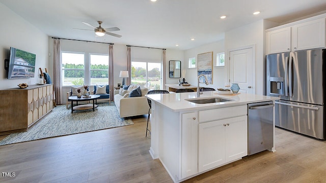 kitchen with appliances with stainless steel finishes, open floor plan, a kitchen island with sink, a sink, and white cabinets