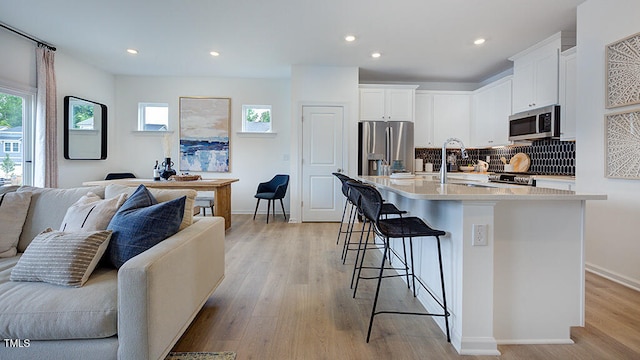 kitchen with appliances with stainless steel finishes, open floor plan, a kitchen island with sink, light countertops, and white cabinetry