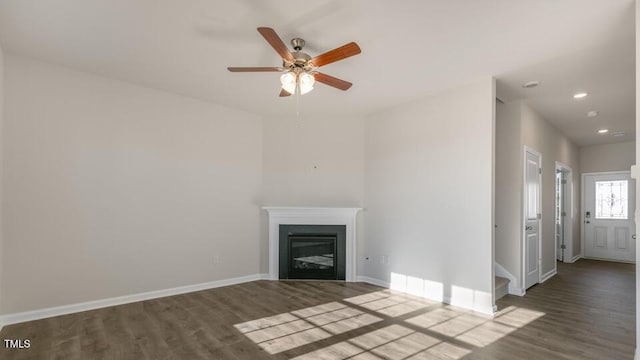 unfurnished living room with recessed lighting, baseboards, dark wood finished floors, and a glass covered fireplace