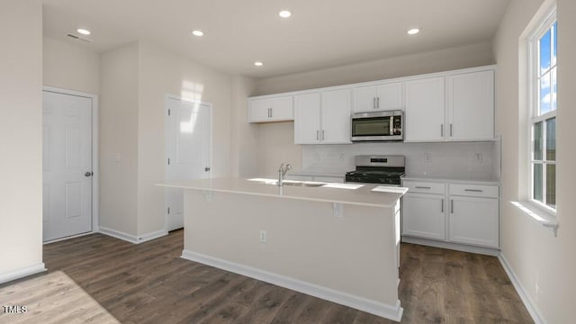 kitchen with light countertops, appliances with stainless steel finishes, white cabinetry, a sink, and an island with sink