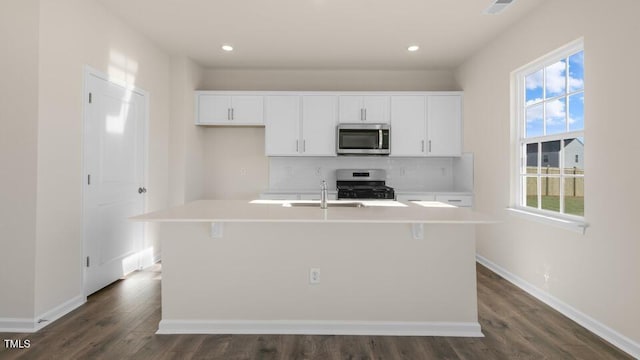 kitchen with range, light countertops, stainless steel microwave, and a center island with sink