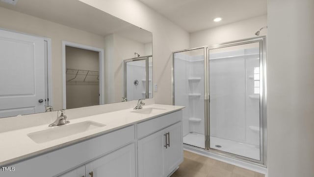 bathroom featuring a sink, double vanity, a stall shower, and a walk in closet